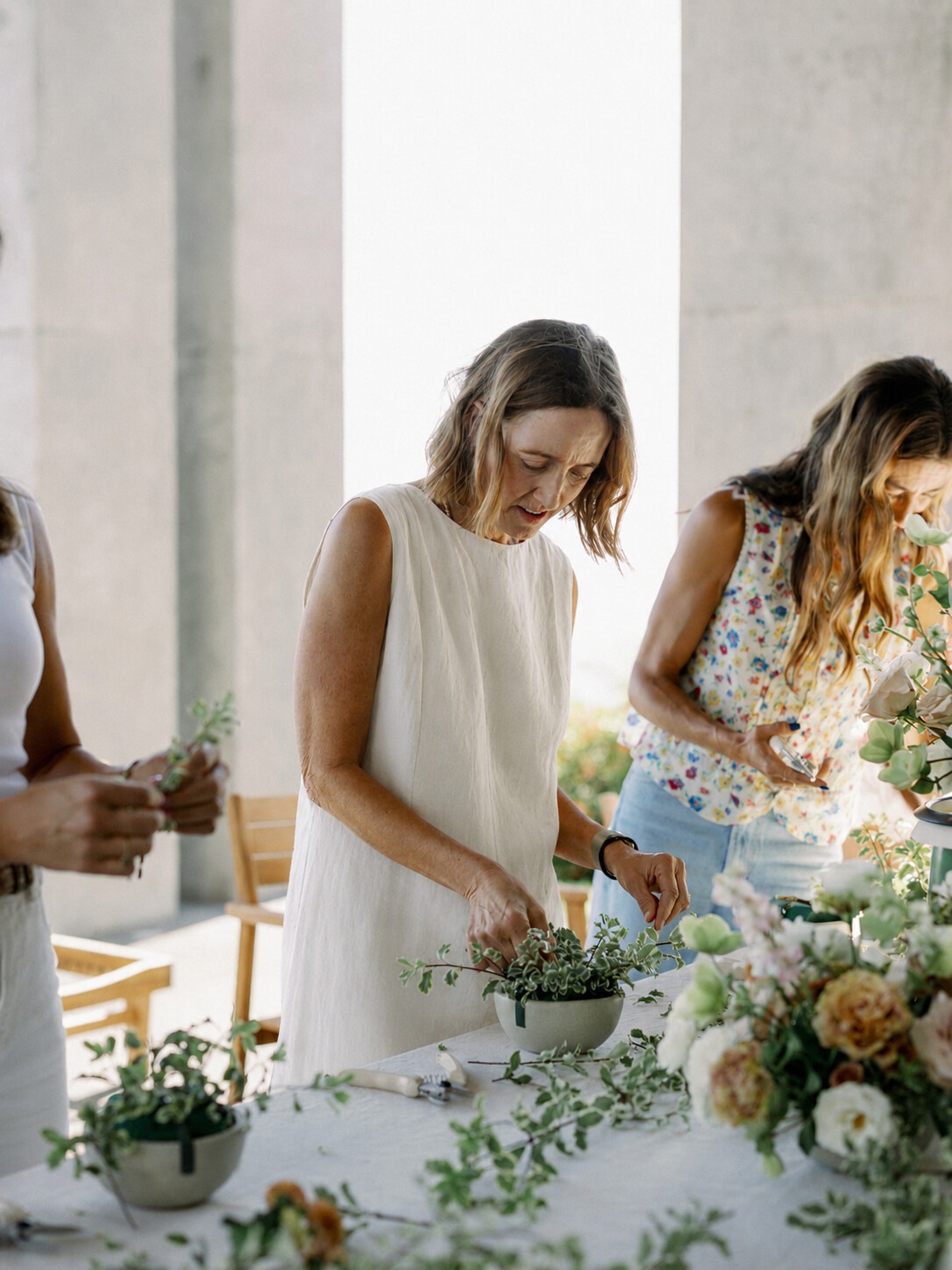 Women arranging wild seasonal flowers at a sunlit retreat table